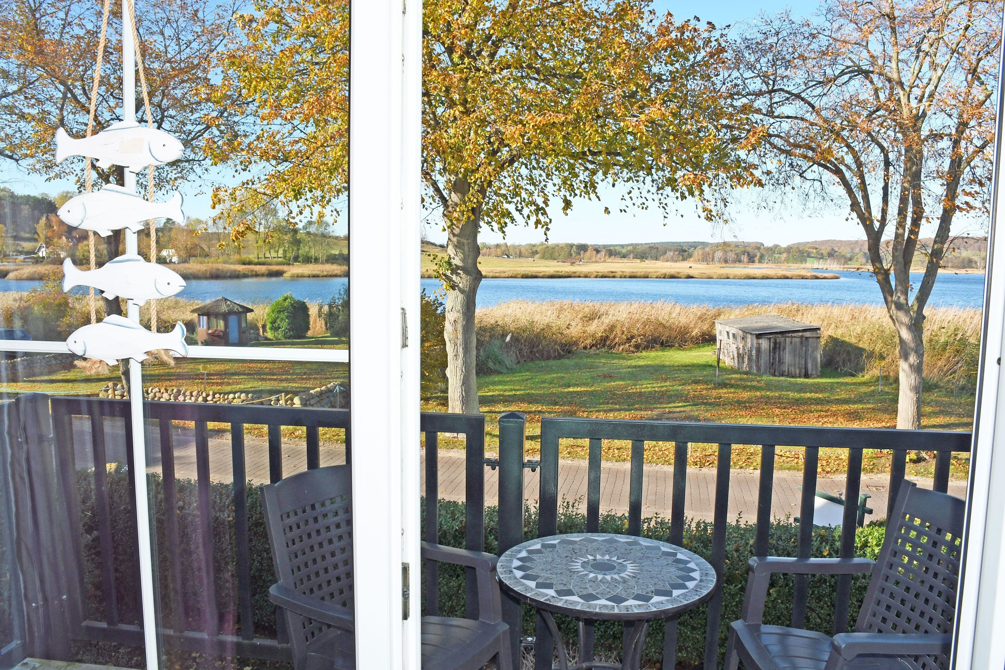 En utsikt från en balkong med ett bord och stolar, med utsikt över en sjö och ett grönområde med träd.