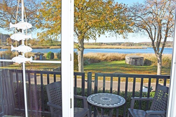 A view from a balcony with a table and chairs, overlooking a lake and grassy area with trees.