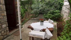 A stone wall, a wooden door, a stone pathway, a round table with a white tablecloth, and a potted plant with red flowers.