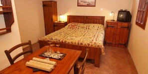Ein kleiner, gemütlicher Raum mit einem hölzernen Bett, einem Tisch mit Gläsern und einer Speisekarte sowie einem Fernseher auf einer Holzkommode.