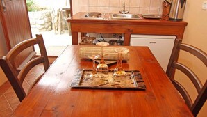 A wooden dining table with chairs, a kitchen area with a sink and stove, and a small refrigerator.