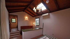A room with a bed, a small kitchenette, a window, and a staircase leading to another room.