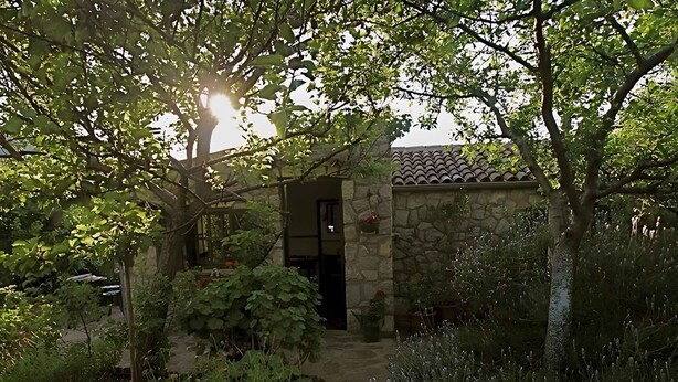 A stone building with a tiled roof, surrounded by lush greenery and a stone pathway leading to the entrance.