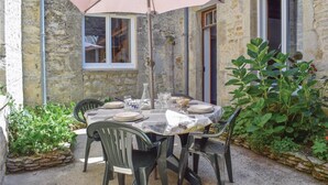 Un área de comedor al aire libre con una mesa preparada para cuatro personas, rodeada de muros de piedra y una sombrilla grande.