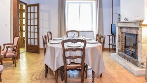 Comedor con una mesa redonda para seis personas, sillas de madera, chimenea y un ventanal con cortinas.