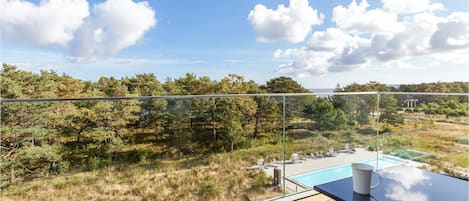 Un balcon avec vue sur une piscine, un espace salon extérieur et une balustrade en verre donnant sur une zone boisée.