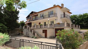 A two-story house with a balcony, a staircase, and a stone wall.