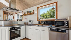 A modern kitchen with white cabinets, stainless steel appliances, a large window, and a wooden ceiling. - Beautiful home in Tarm with sauna (Tarm)