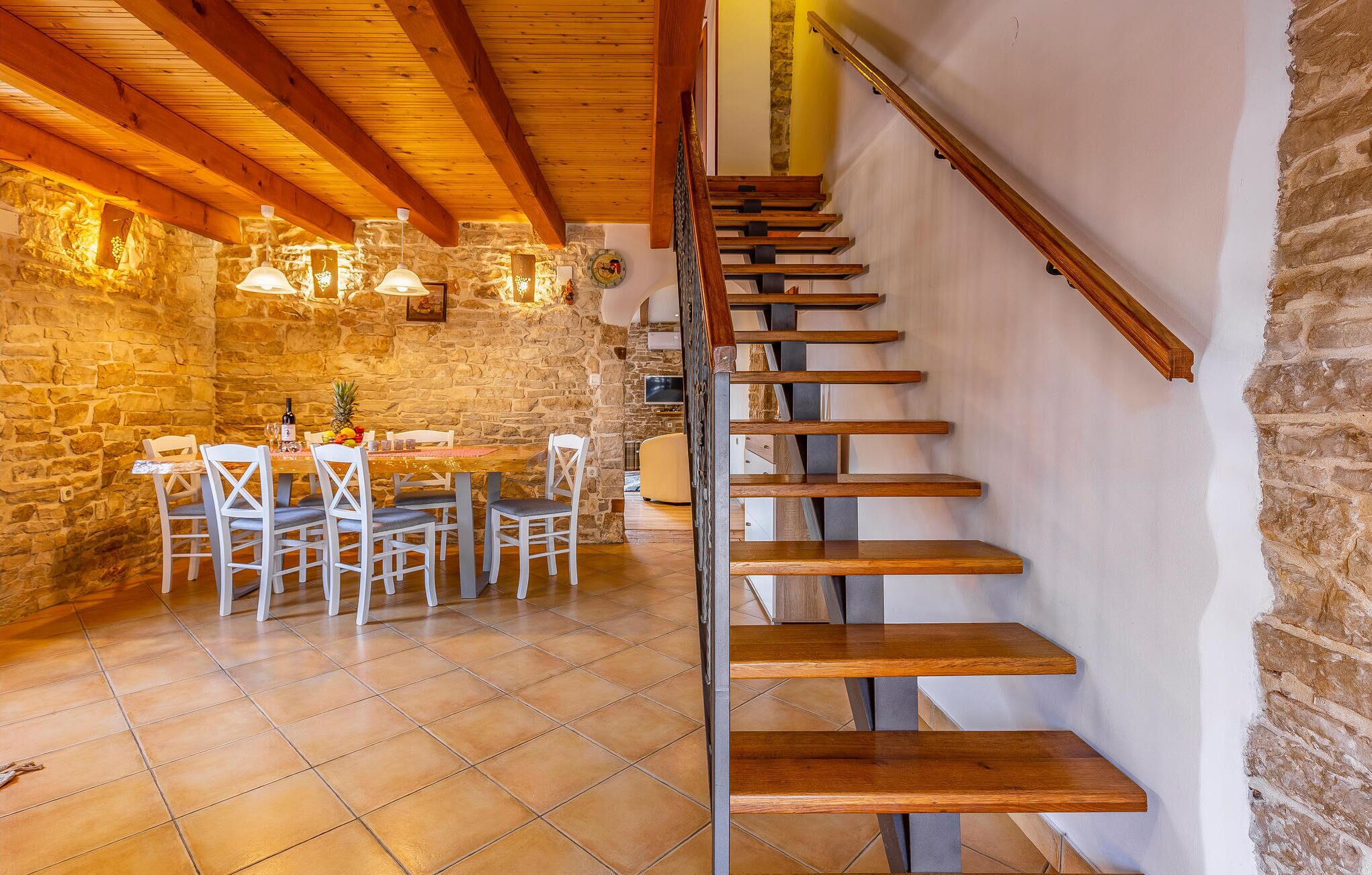 A dining area with a stone wall, wooden ceiling beams, and a staircase with wooden steps.
