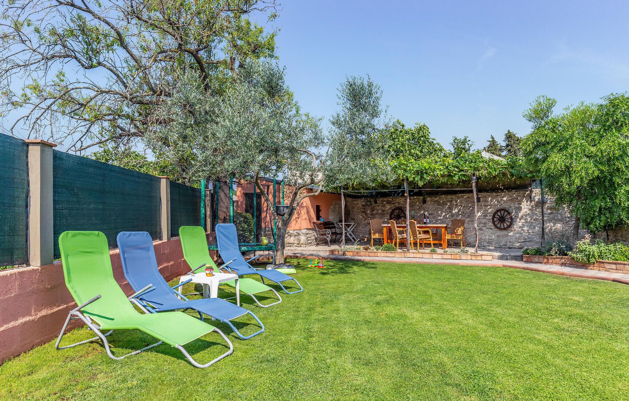 Une terrasse avec des fauteuils de jardin verts, une table et un mur en pierre.