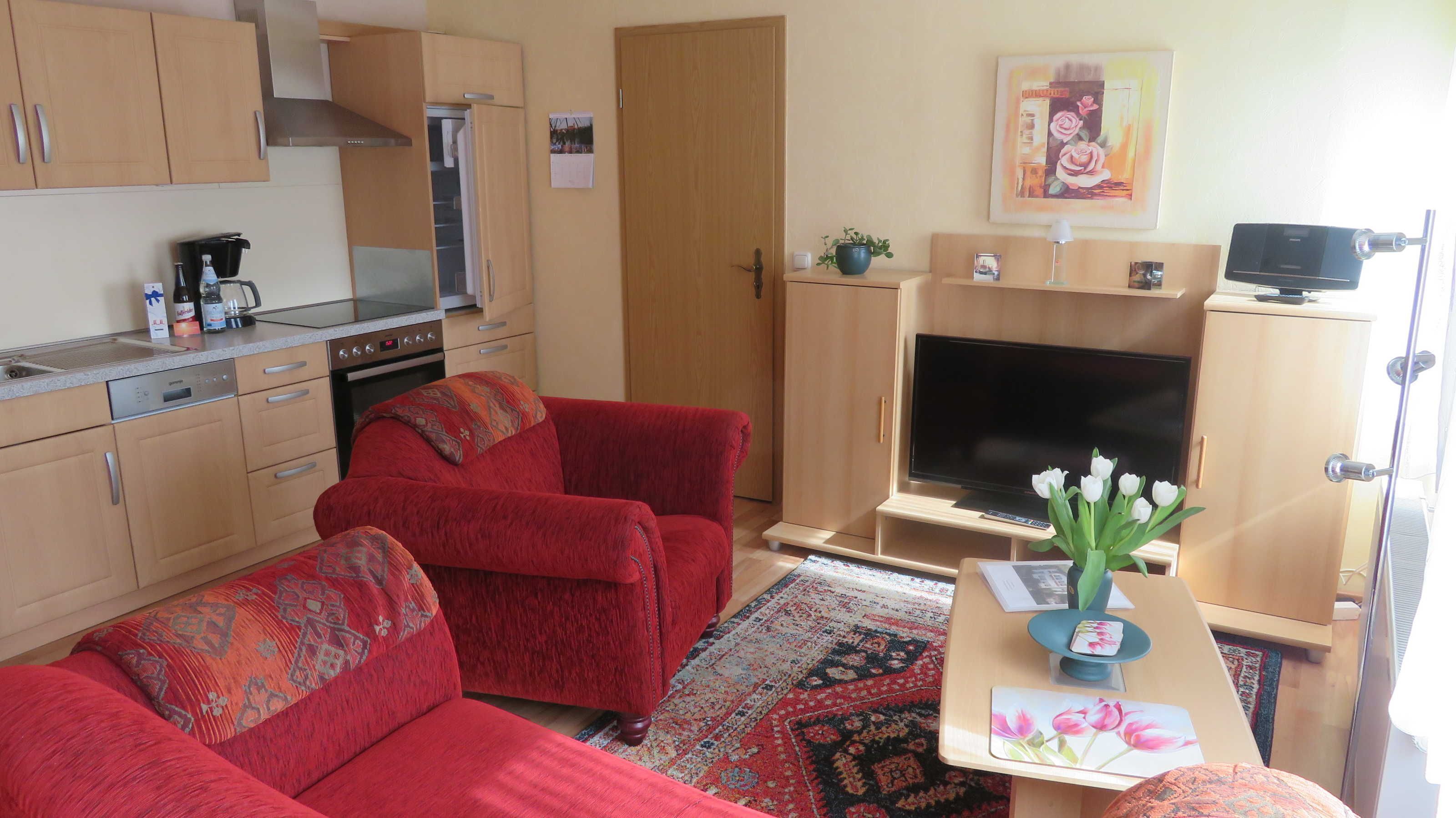 Un espacio habitable compacto con kitchenette, un sofá, un televisor y una pequeña mesa con un florero.