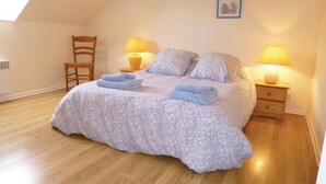 Camera da letto con soffitto spiovente, un letto con copriletto floreale, due lampade da comodino, una sedia e un tavolino con lampada.