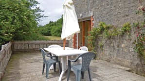 Un patio esterno con tavolo e sedie, un ombrellone bianco e un muro in pietra.