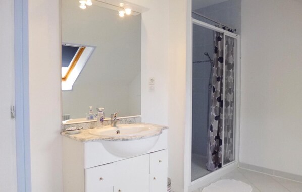 Un baño con lavamanos, espejo y ducha blancos.