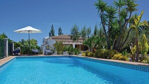A swimming pool with a geometric tile pattern, surrounded by palm trees and a building with a tiled roof. - Lovely home in Alcúdia (Alcúdia)