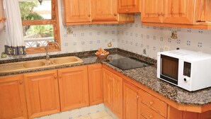 A kitchen with wooden cabinets, a granite countertop, a sink, and a microwave. - Lovely home in Alcúdia (Alcúdia)