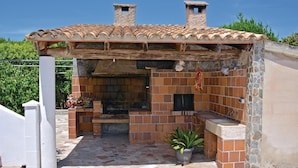An outdoor brick barbecue area with a tiled roof, stone chimneys, and a potted plant. - Lovely home in Alcúdia (Alcúdia)