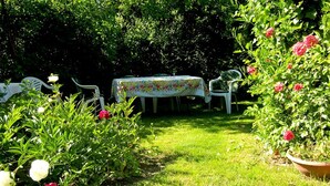 A garden with a table and chairs, surrounded by lush greenery and flowering plants.