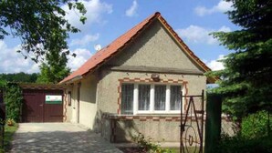 A single-story house with a red-tiled roof, a small porch, and a gated entrance.