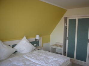 A bedroom with a bed, pillows, a nightstand, a lamp, and a wardrobe. - Vacation home Hiddensee on the Baltic Sea - Apartment III (Meeresrauschen) (Insel Hiddensee)