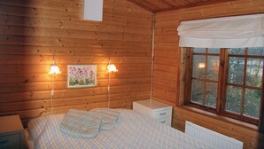 Une chambre à coucher dans une cabane en bois, avec un lit, deux lampes de chevet, une fenêtre avec des rideaux et un radiateur.