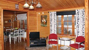 L’intérieur d’un chalet en bois comprend un coin repas, un téléviseur et des chaises rouges.