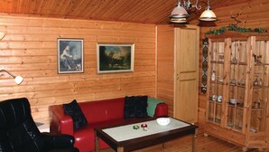 L’intérieur d’un chalet en bois, avec un canapé rouge, un meuble en bois doté de portes en verre et deux tableaux encadrés accrochés au mur.