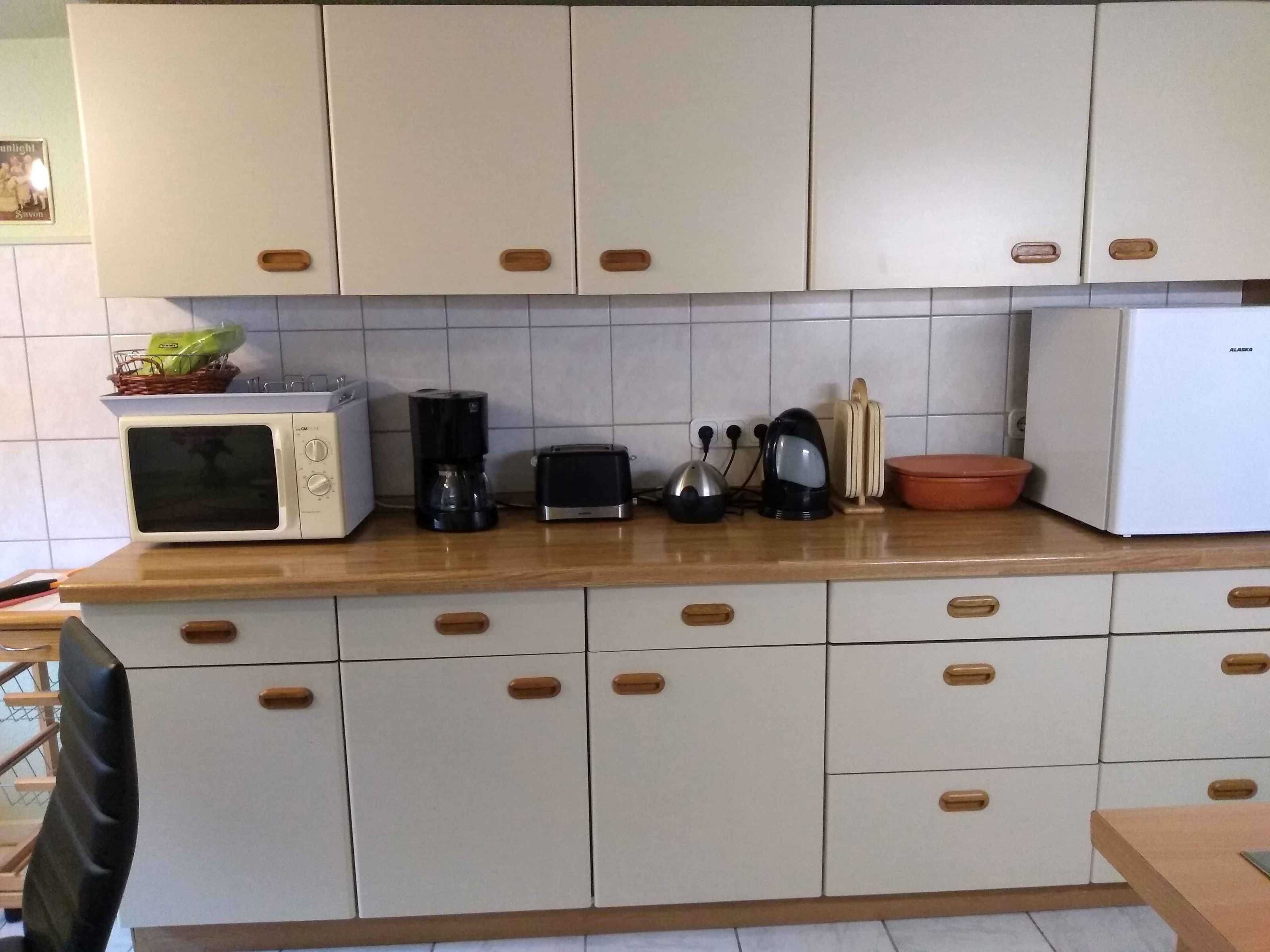 A kitchen with white cabinets, a microwave, a toaster, a kettle, and a refrigerator.