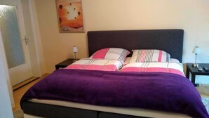 Una camera da letto con un letto, due comodini, una porta e un quadro appeso al muro.