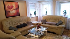 Un soggiorno con due divani beige, un tavolino in vetro e un grande quadro astratto appeso al muro.