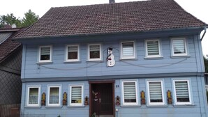 Un edificio a due piani con tetto in tegole, diverse finestre con persiane e un portone d'ingresso con un piccolo portico.