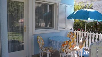 A patio with a table and chairs, a white picket fence, and a blue umbrella.