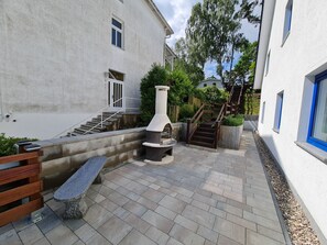 A courtyard with a stone bench, a fireplace, and a staircase leading to a door.