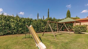 Ein Spielplatz mit Rutsche und Schaukeln in einer grünen Rasenfläche, umgeben von Hecken und einem Gebäude mit Gründach.