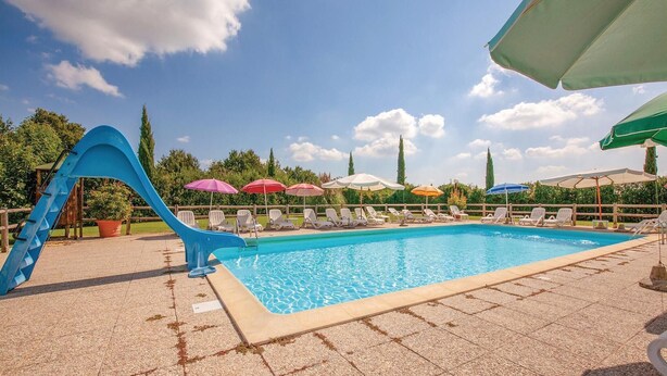 Ein Swimmingpool mit blauer Rutsche, umgeben von Liegestühlen und Sonnenschirmen.