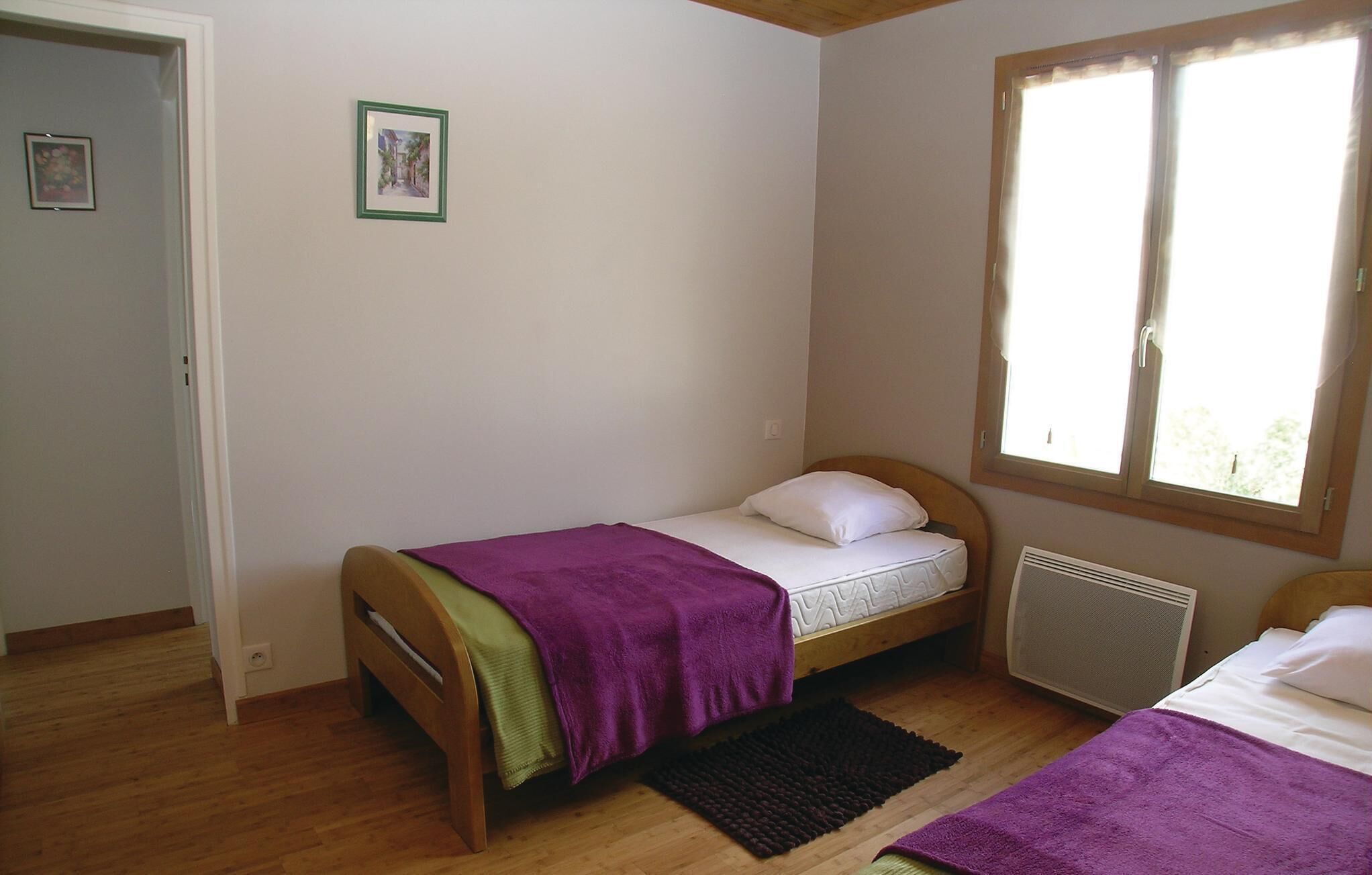 Une petite chambre avec un lit simple, un plancher en bois, une fenêtre avec des rideaux, un radiateur et une porte.