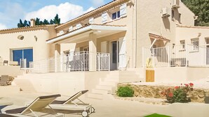 Ein zweistöckiges Gebäude mit Balkon, Tür und einem kleinen Garten mit Blumen.
