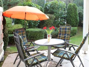 Une terrasse avec une table ronde, quatre chaises, un parasol orange et un vase rempli de fleurs rouges.