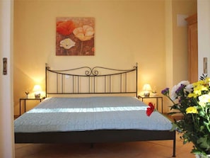 Un lit avec un cadre en métal, deux lampes de chevet, un tableau floral accroché au mur et un vase rempli de fleurs.
