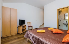 Ein Schlafzimmer mit Bett, Fernseher, Stuhl, Kleiderschrank und einem Badezimmer mit Waschbecken und Spiegel.