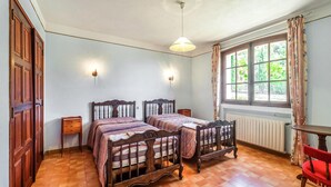 A bedroom with two wooden beds, a window with curtains, a radiator, and a red chair. - Domaine de la Bastide d'Agay (Agay)