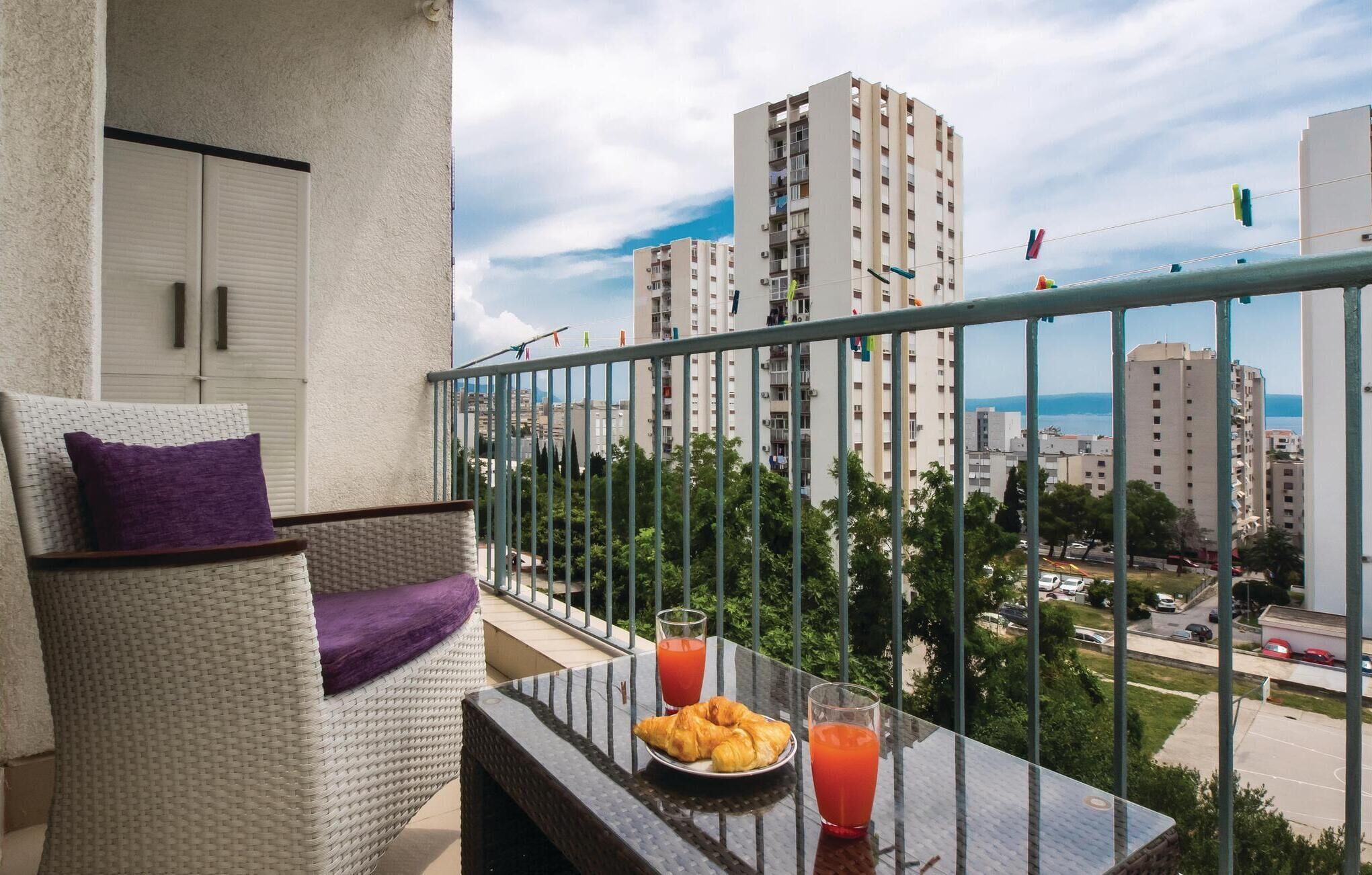 A balcony with a wicker chair, a plate of croissants, and two glasses of orange juice.