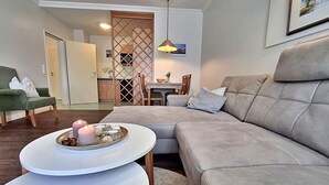 Un salon moderne avec un canapé gris, une table basse blanche ornée d’une bougie, et un coin repas à l’arrière-plan.