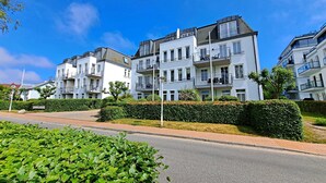 Un immeuble d’appartements moderne doté de nombreux balcons, d’un jardin bien entretenu et surplombant un ciel d’un bleu éclatant.