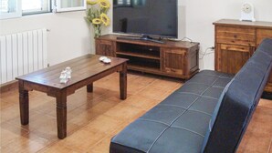 Een woonkamer met een houten salontafel, een bank, een televisie op een houten dressoir, een vaas met zonnebloemen en een klok op een kast.