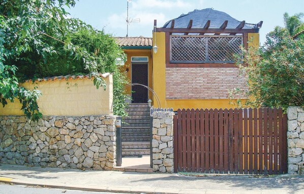 Una casa amarilla con un muro de piedra, un portón de madera y una escalera que lleva a la entrada.