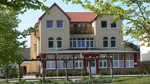 Un bâtiment à deux étages, doté d’une façade rouge et blanche, d’un balcon et portant l’inscription « Villa Meeresrauschen » sur la façade.