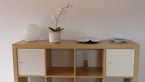Une console en bois surmontée d’un vase blanc, d’une orchidée en pot et d’un bol décoratif.