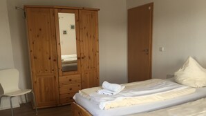 Une chambre avec une armoire en bois, un lit simple avec du linge de lit blanc et une chaise blanche.