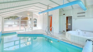 Una piscina interior amb aigua cristal·lina, una banyera d'hidromassatge i una zona de terrassa coberta amb cadires.